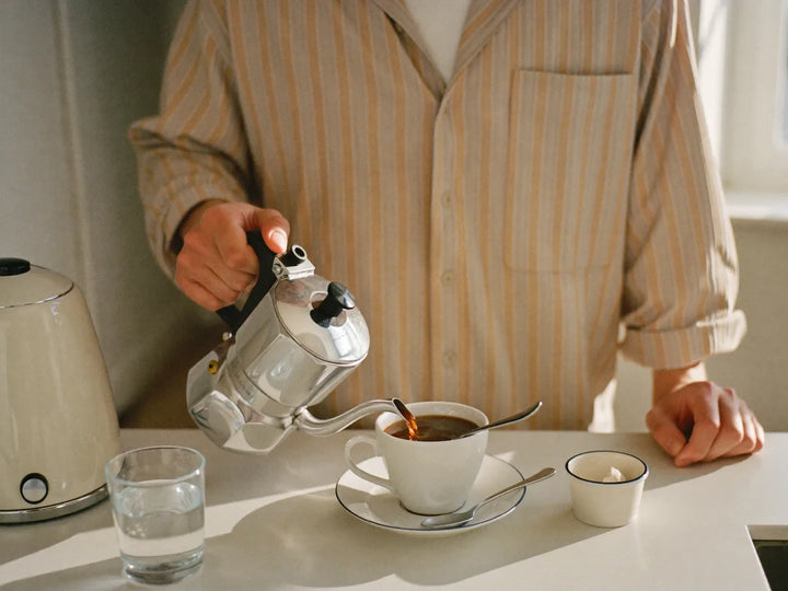 Man making coffee in a bright kitchen with a glass of water on the counter