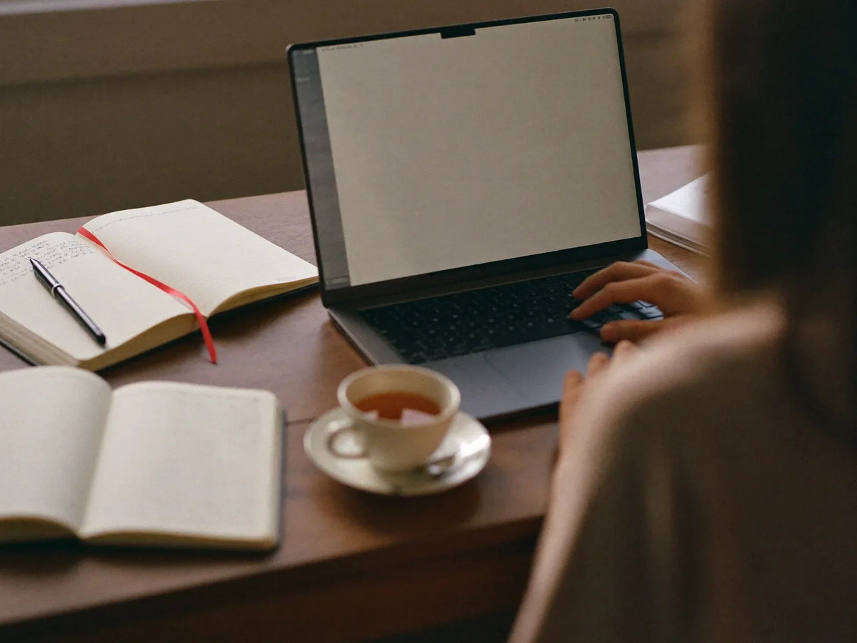 Person researching at a desk with a laptop, notebooks and a cup of tea