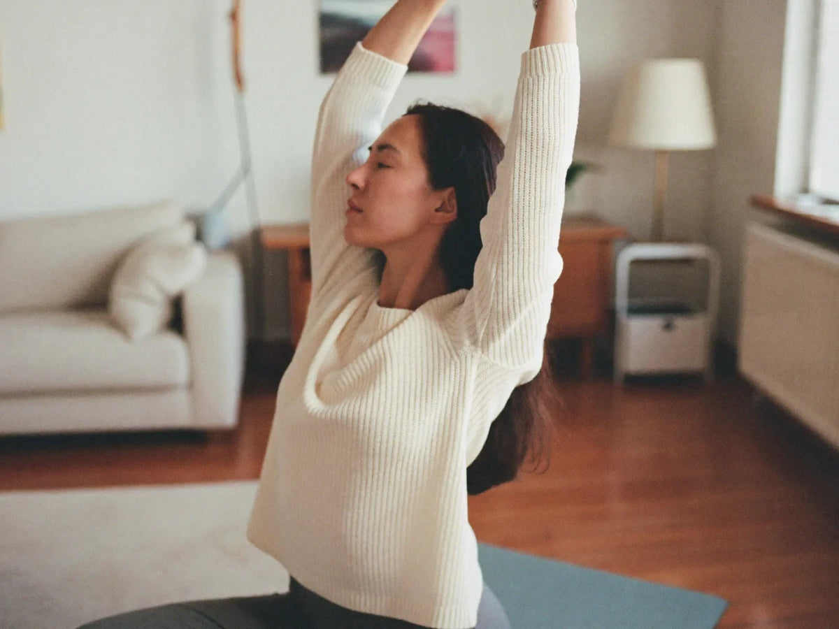 Woman stretching on a yoga mat in a bright living room in the morning