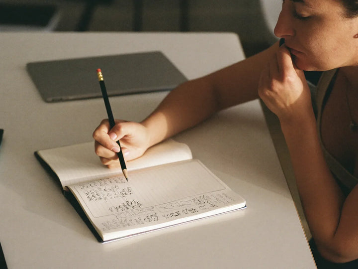 Woman at a desk ticking off a handwritten checklist in a notebook