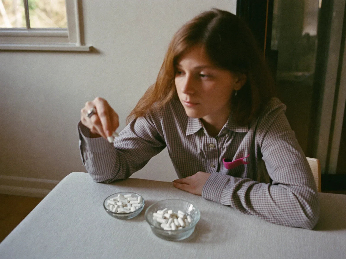 Woman at a kitchen table comparing a dish of tablets and a dish of capsules